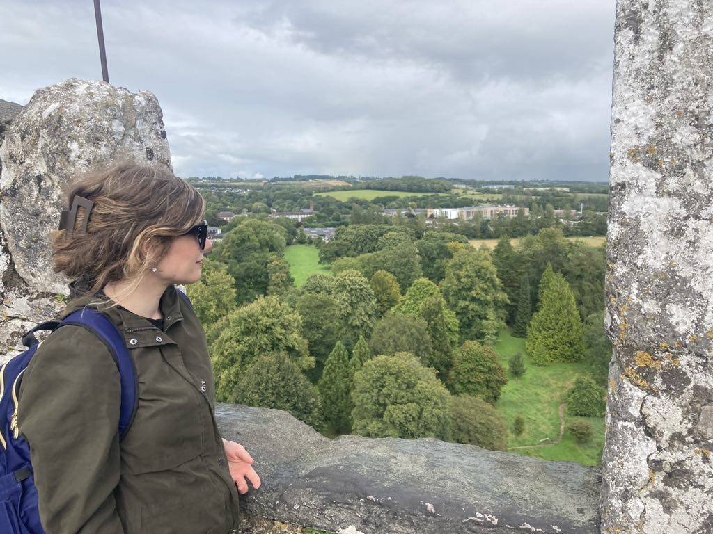 Lindsay Renaud standing on a stone structure, overlooking a lush green landscape, symbolizing self-reflection and personal growth.