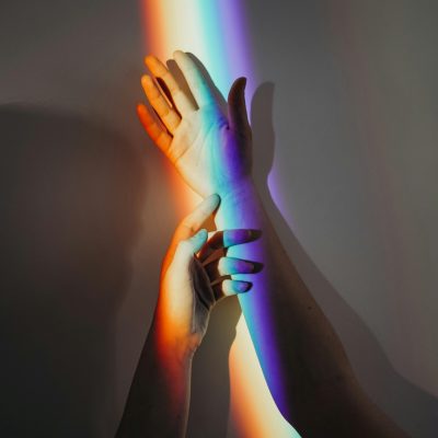 A beautiful display of rainbow light casting on intertwined hands symbolizing unity and love.