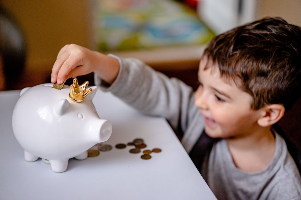 Smiling child placing a coin into a piggy bank, symbolizing financial savings and affordable therapy options for families.