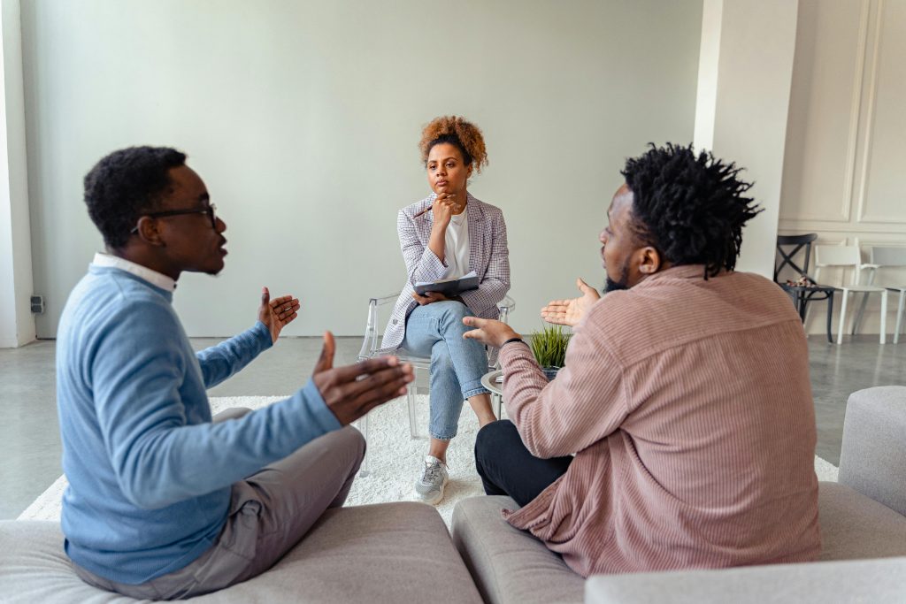 A therapist listens as a couple engages in discussion during a counselling session, working on communication and conflict resolution.